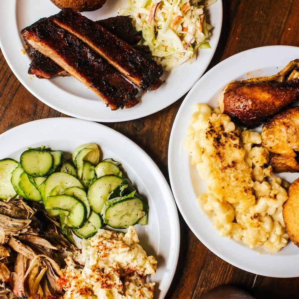 Three plates of barbecue food, including ribs, pulled pork, chicken, mac and cheese, coleslaw, and pickles.