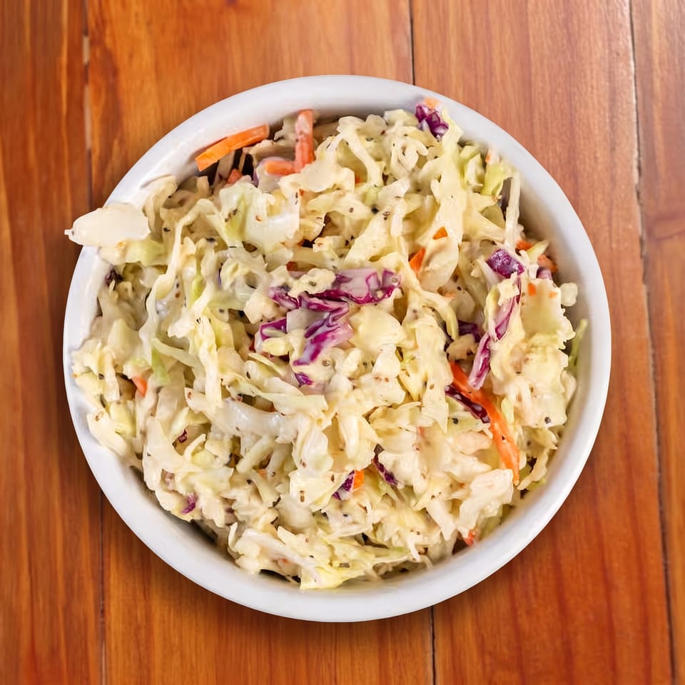 Creamy pasta salad with cabbage, carrots, red cabbage, and herbs in a white bowl on a wooden table.