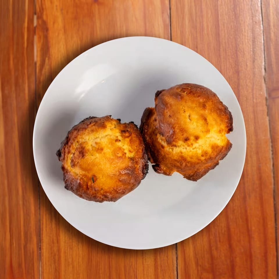 Two golden-brown baked pastries sit on a white plate atop a wooden table.