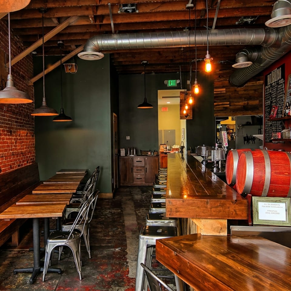 Rustic restaurant interior with brick walls, wooden tables, a long bar, and red beer barrels.