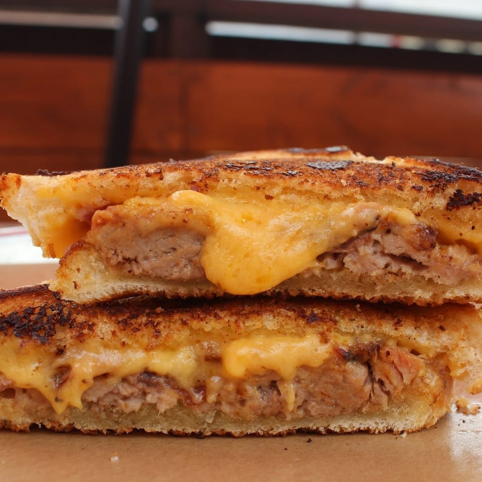 Close-up of a grilled cheese sandwich stacked with savory sausage patties and melted cheddar on toasted bread.