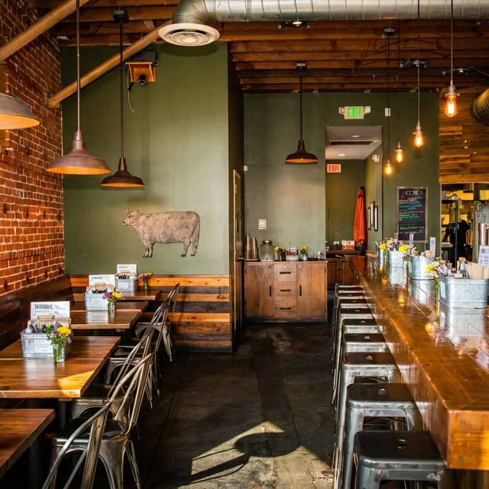 Rustic restaurant interior with brick walls, wooden tables, a long bar, and industrial lighting.