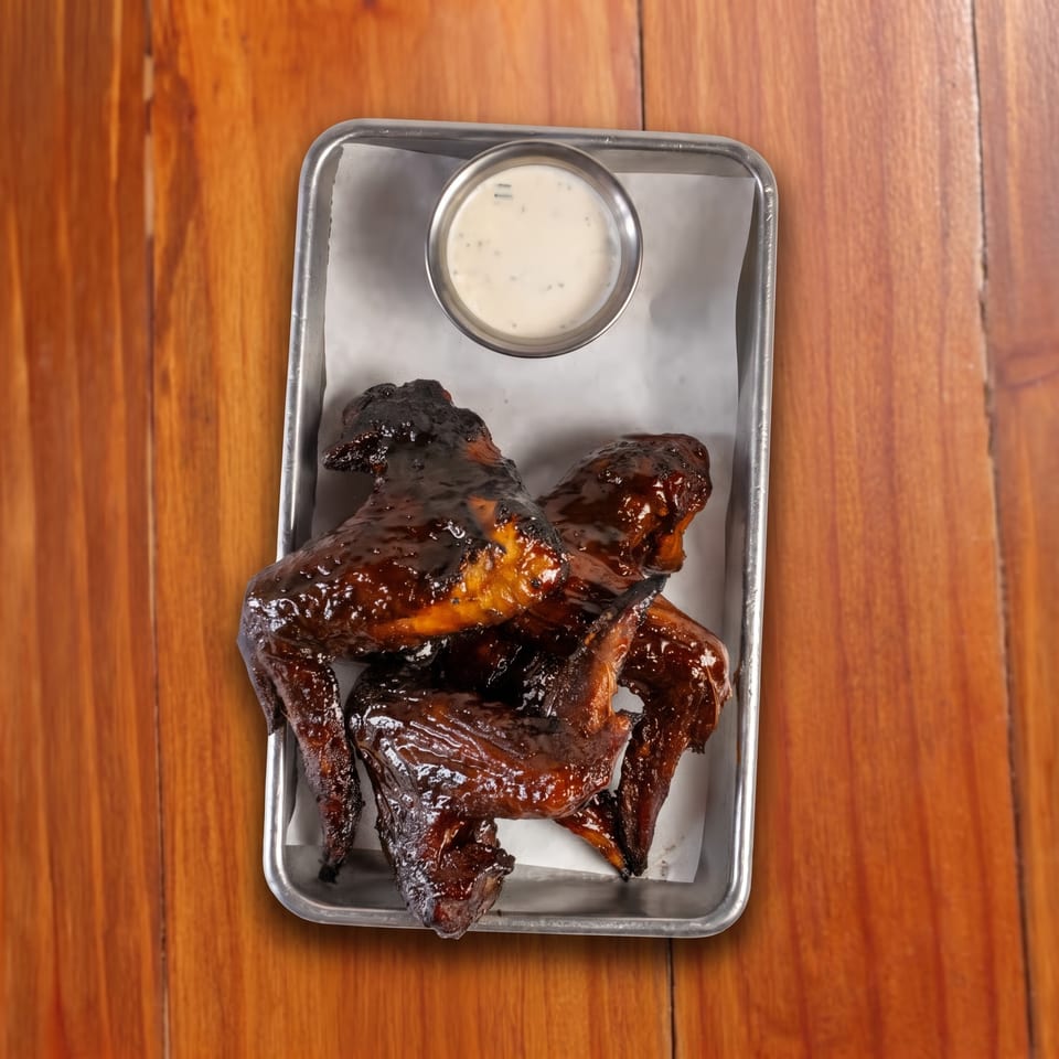 Glazed barbecue chicken wings served with creamy dipping sauce on a metal tray atop a wooden table.