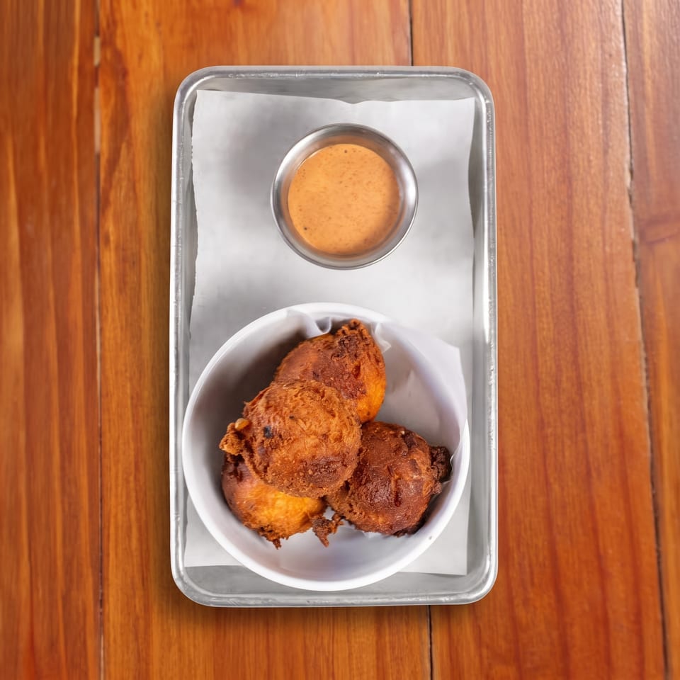 Overhead view of fried chicken pieces in a white bowl with dipping sauce on a metal tray atop a wooden table.
