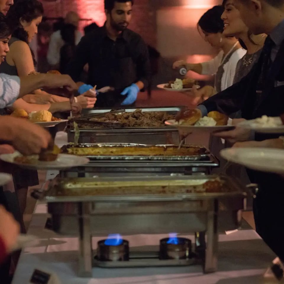 Guests serve themselves from steaming buffet trays during a lively restaurant gathering.