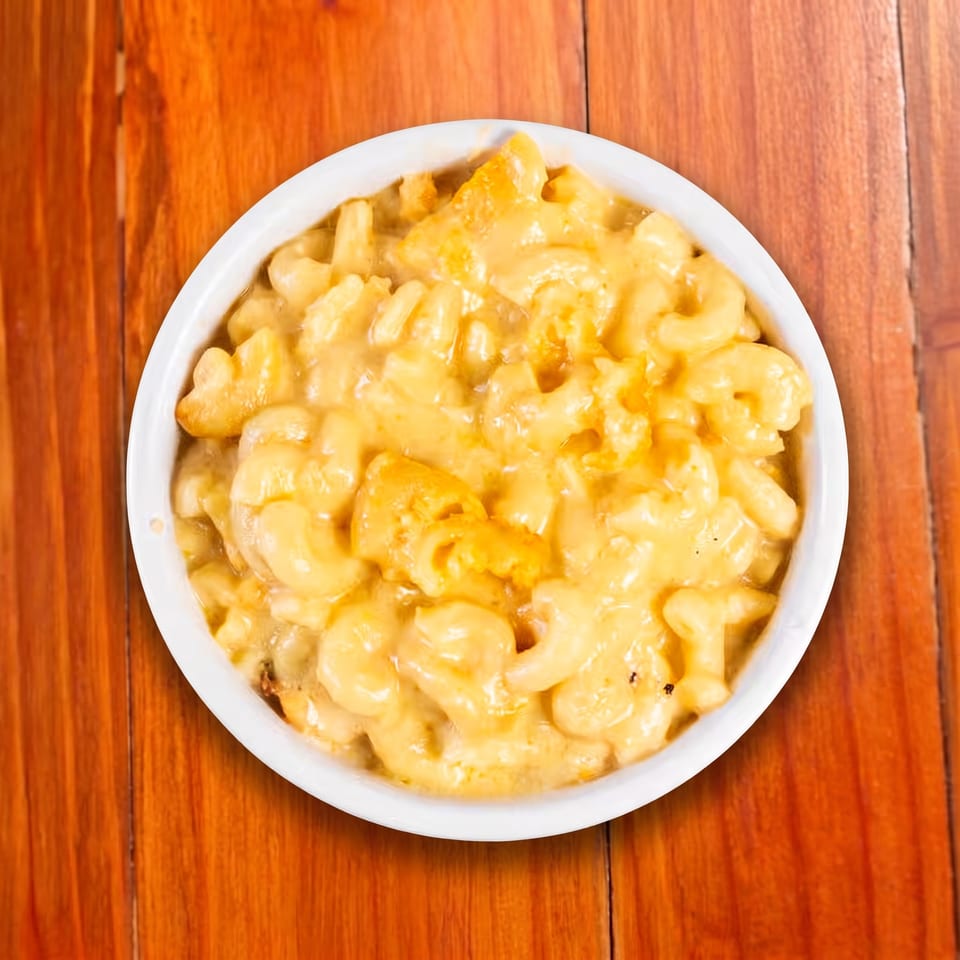 Bowl of creamy, golden macaroni and cheese on a warm wooden table.